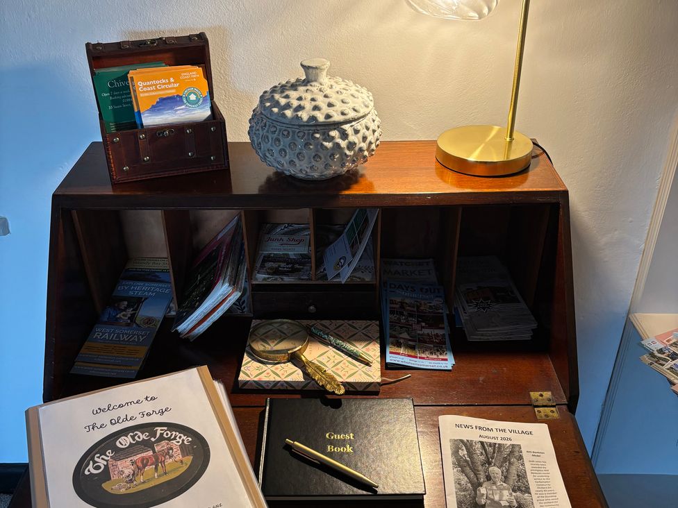 A lobby with a wooden table, guest book and lamp at The Olde Forge in Carhampton near Minehead