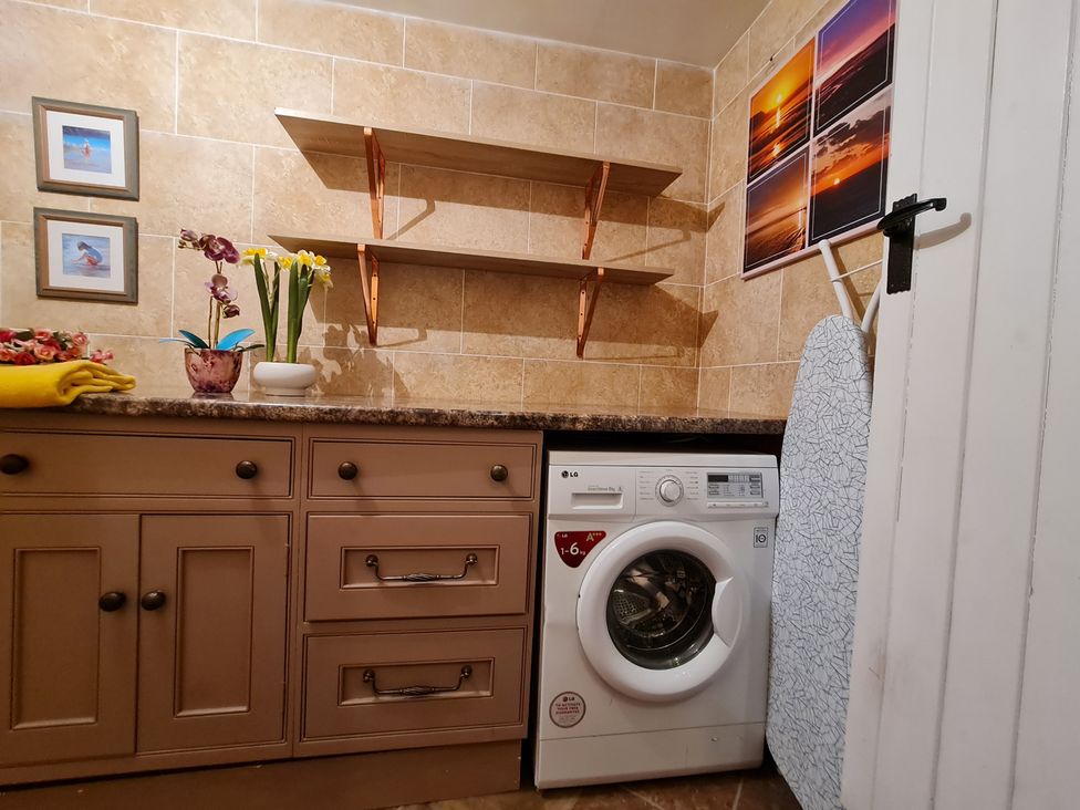 A laundry room with a washing machine, shelves, and storage at Sea view cottage in Penmaenmawr