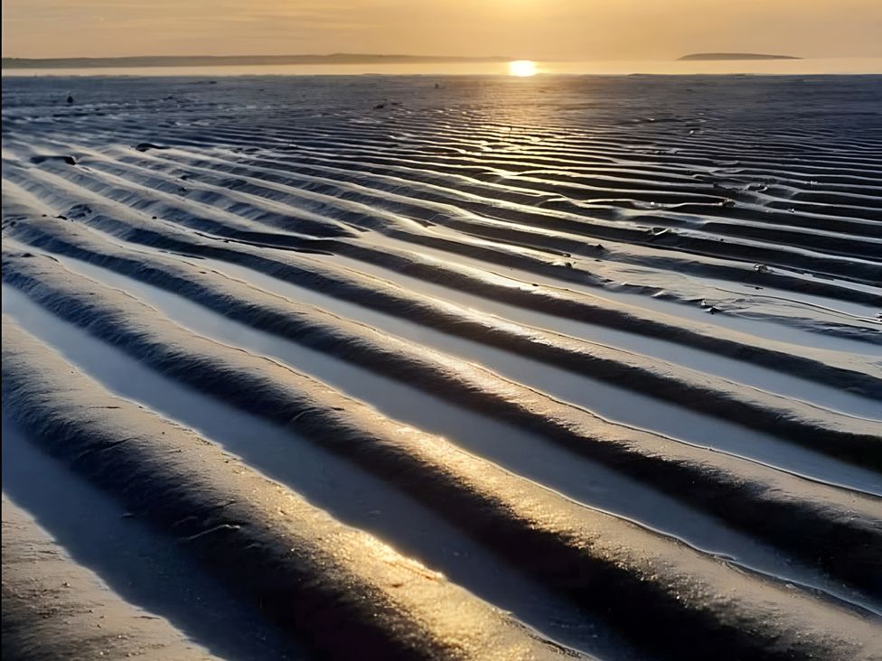 A sandy beach with water and sunset at Sea view cottage in Penmaenmawr