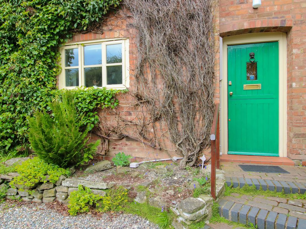 A green door and window on a brick wall with plants at Cardington 25