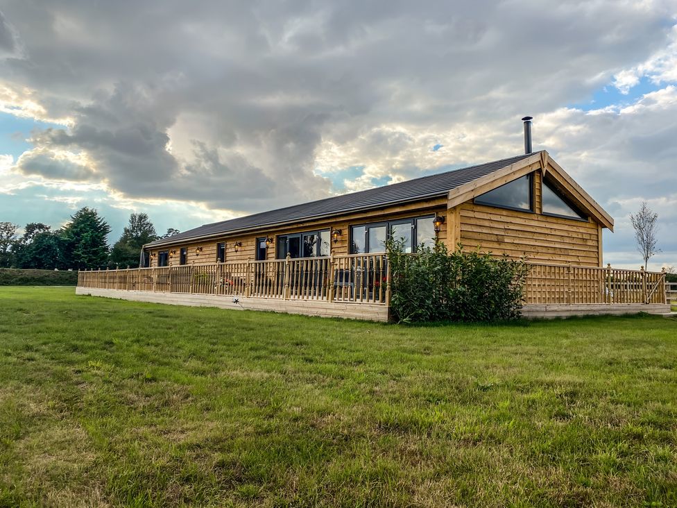 A wooden lodge with a deck and grass area at Fox Lodge in York