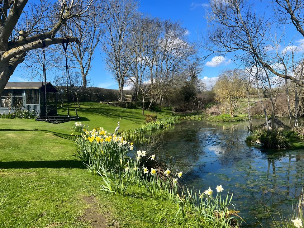 A garden with a swing, shed, and pond at Christmas Cottage in Shipston-on-Stour