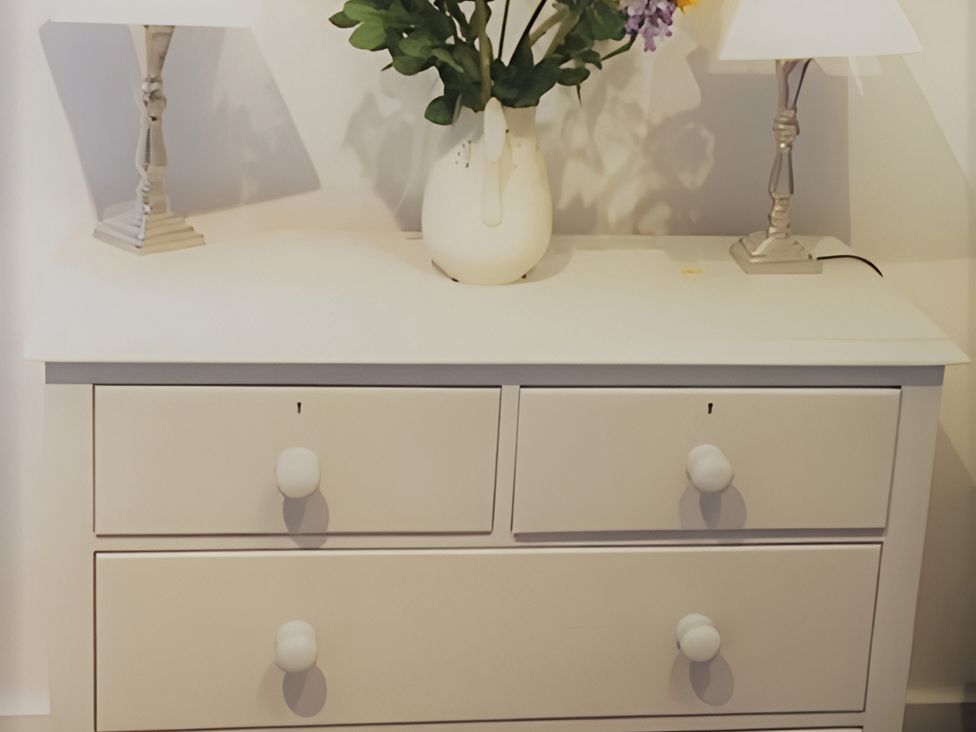 A dresser with a vase of flowers and lamps at Loxley Barn in Tring