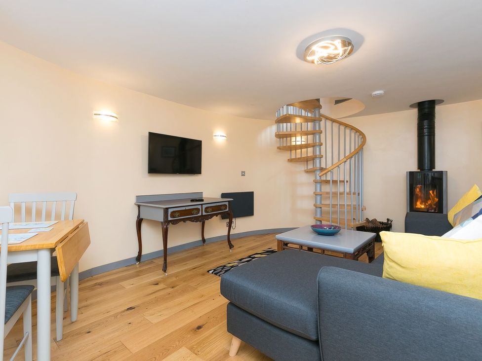 A living room with a sofa, coffee table, and spiral staircase at The Old Well House in Redruth