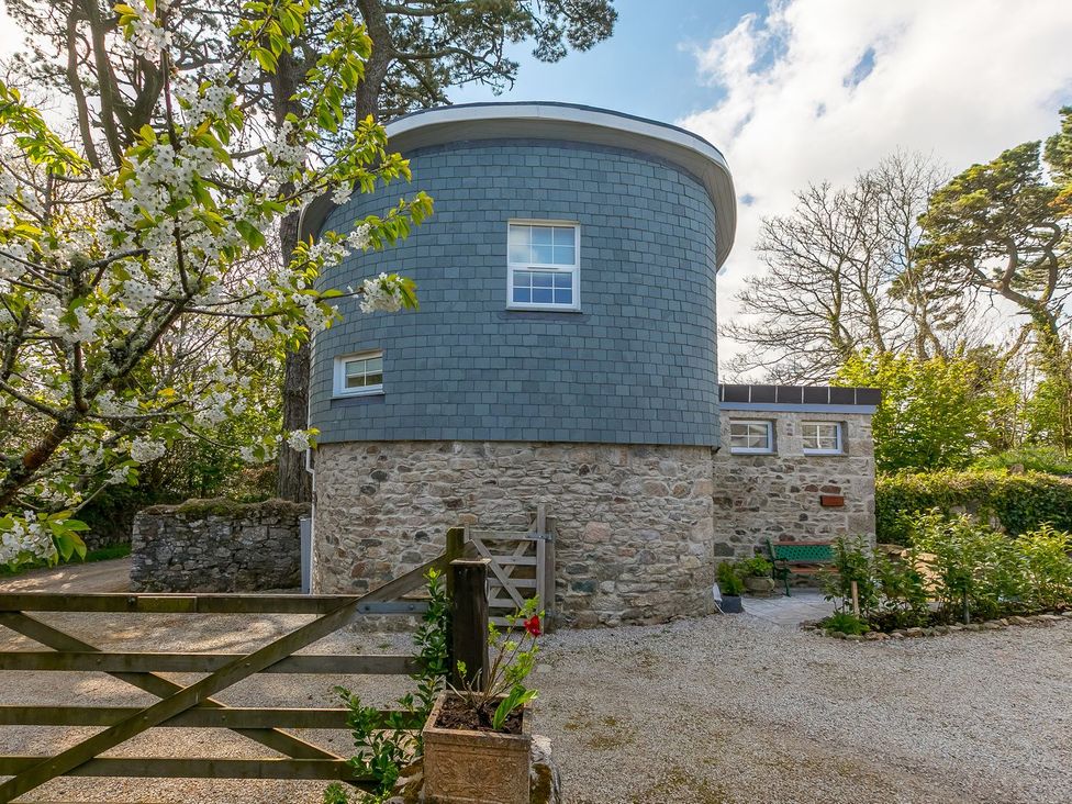 A round building with stone walls and windows in an outdoor area at The Old Well House in Redruth