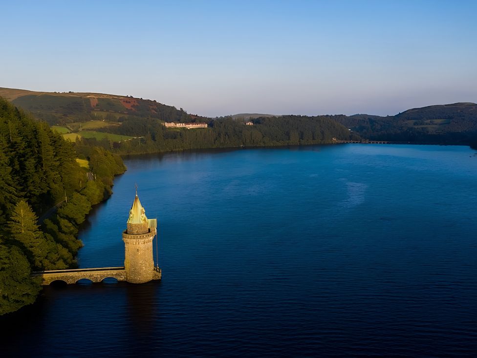 A lake with a tower and forest surrounding it at Honey Bee Cottage Welshpool