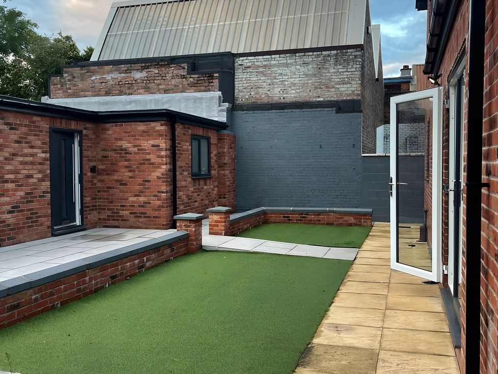 A garden area with a lawn and paving stones at Citrine Suite in Stoke-on-Trent