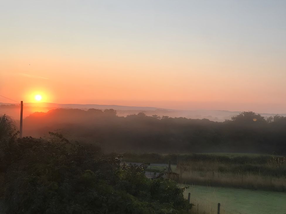 A sunrise over a misty field with trees at Shepherds hut Dumfries