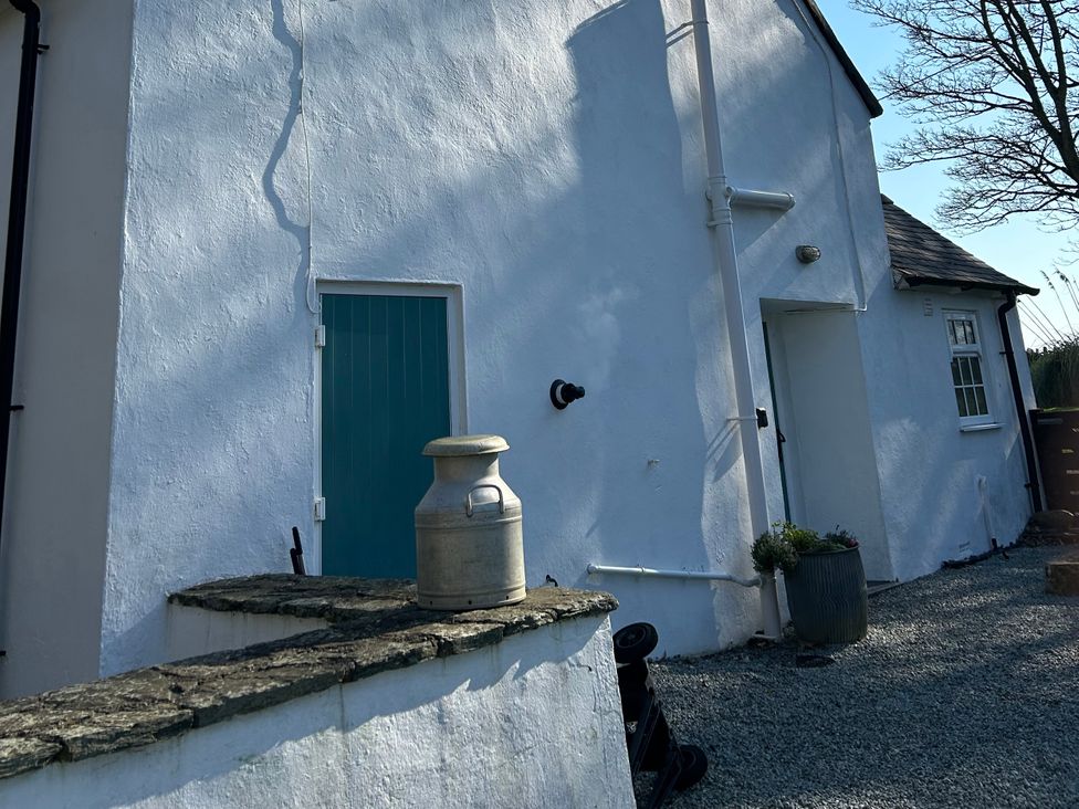An exterior view showing a wall with a door and a milk jug at Bodior Garden Cottage Bach Rhoscolyn