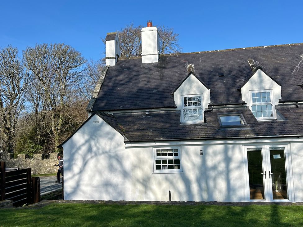 A white cottage exterior with a pathway and trees at Bodior Garden Cottage Bach Rhoscolyn