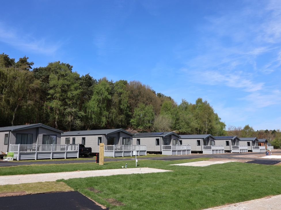 A row of cabins with wooden decking in a park at No.6 - The Pines, Delamere