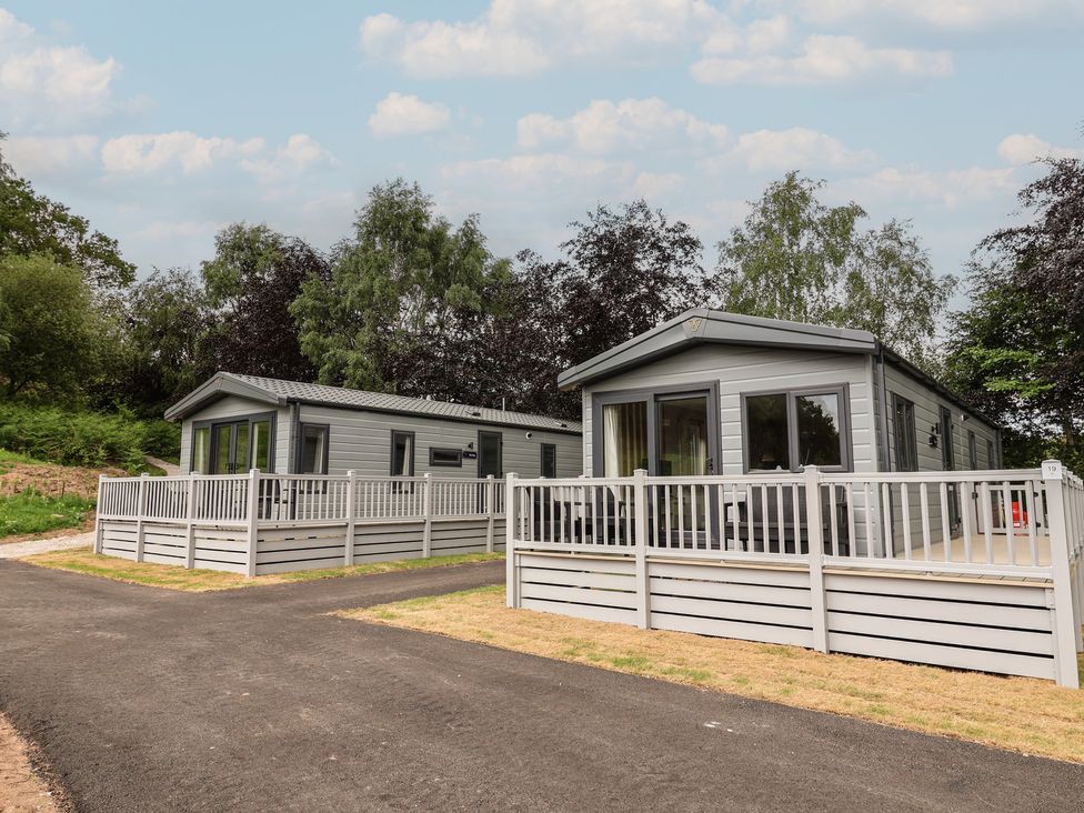 Two park homes with fences and trees in an outdoor area at The Pines 3 Bedrooms Delamere