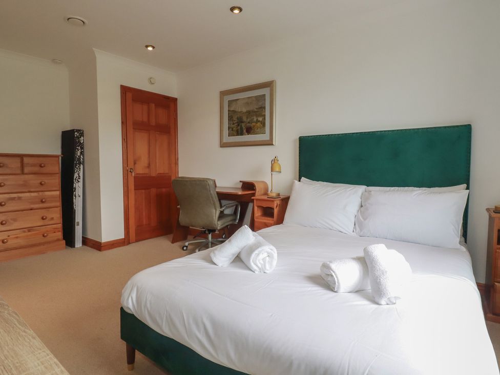 A bedroom with a green headboard and a wooden desk at Beachcombers Apt 11 
