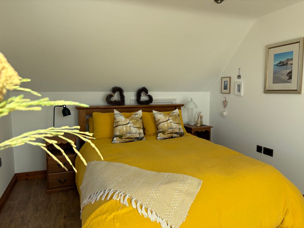A bedroom with a yellow bedspread and nightstand at Lowenna Watergate Bay near Newquay