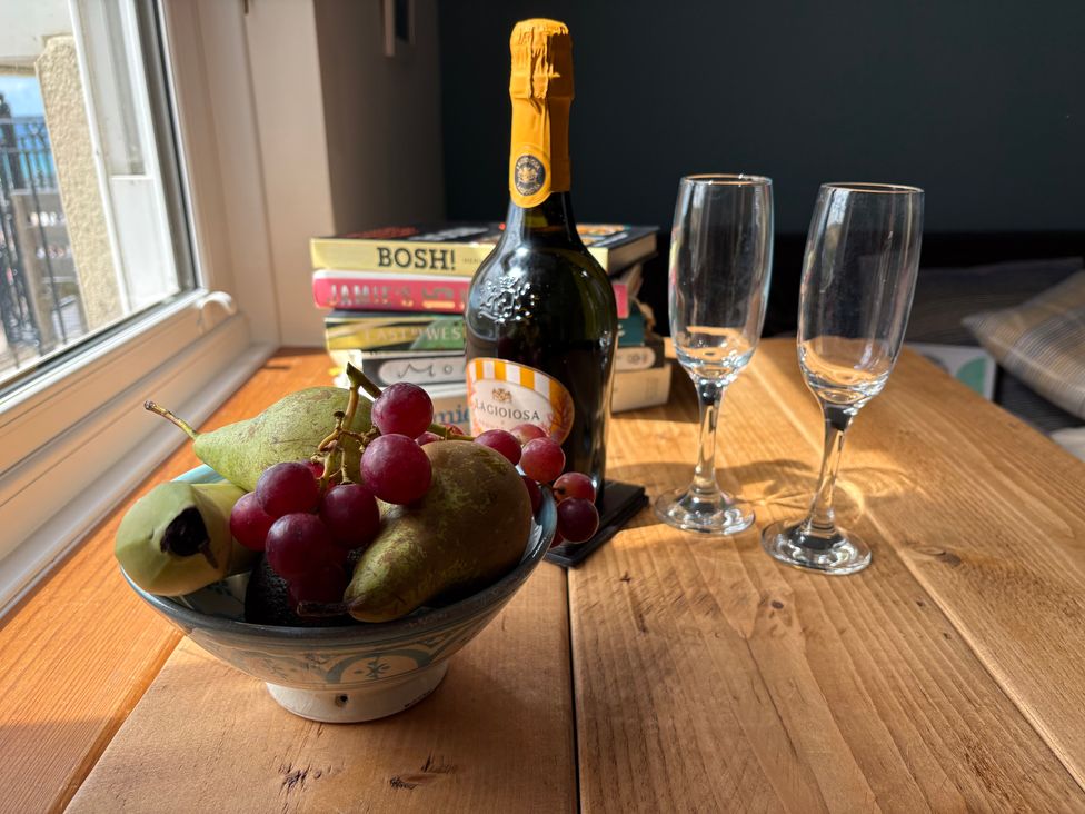A bowl of fruit, champagne bottle, and glasses on a table at Lowenna in Watergate Bay near Newquay
