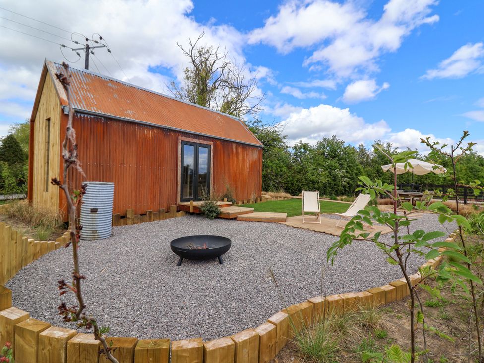 A garden with a shepherd's hut, fire pit, and seating area at Shades Farm Shepherds Hut in Circenester