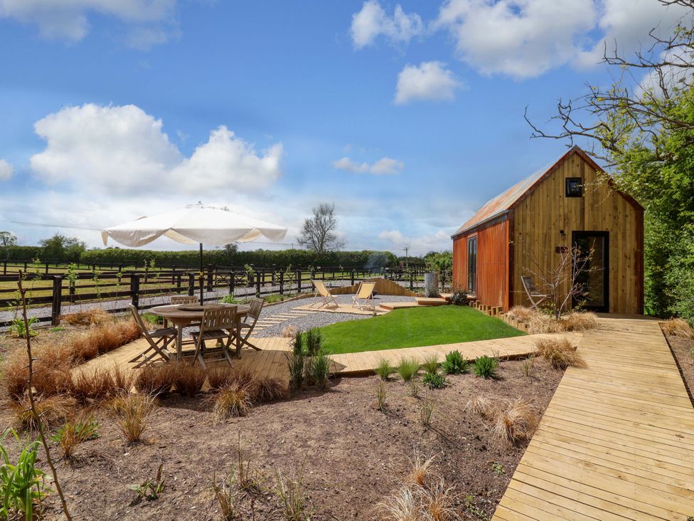 An outdoor area with a wooden hut, table, chairs, and umbrellas at Shades Farm Shepherds Hut (Sleeps 4) Cirencester