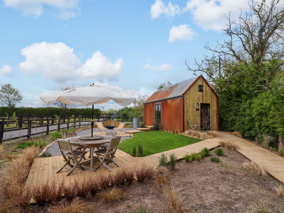 An outdoor area with a hut, table, chairs, and umbrella at Shades Farm Shepherds Hut (Sleeps 4) Cirencester