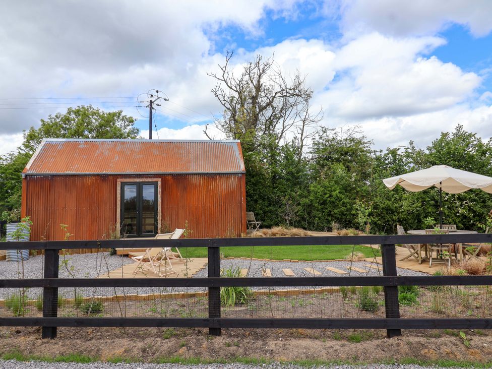 A shepherd's hut with a wooden deck and gravel path at Shades Farm Shepherds Hut (Sleeps 4) Circenester