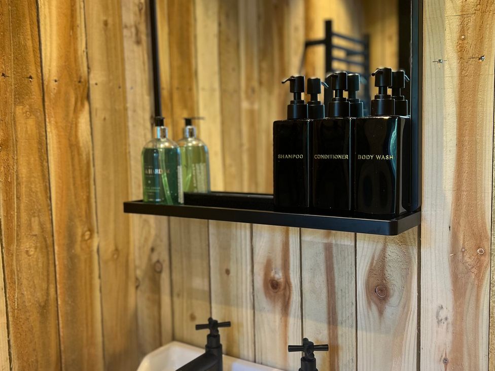 A bathroom with a sink and shelves containing shampoo, conditioner, and body wash at Rustwood Manor in Minety