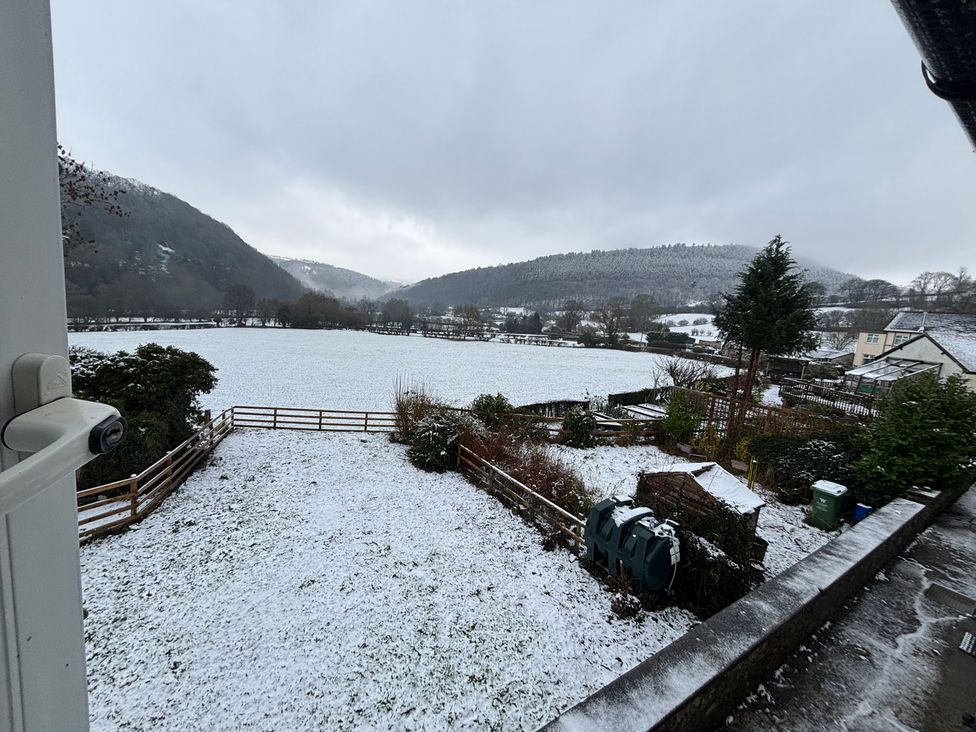 A snow-covered field with trees and hills at Araelfa in Llwynmawr