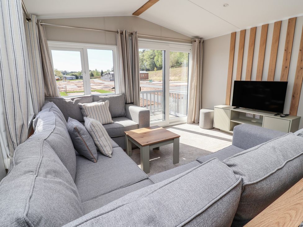 A living room with a sofa, TV, and large windows at No.20 - The Oaks in Delamere