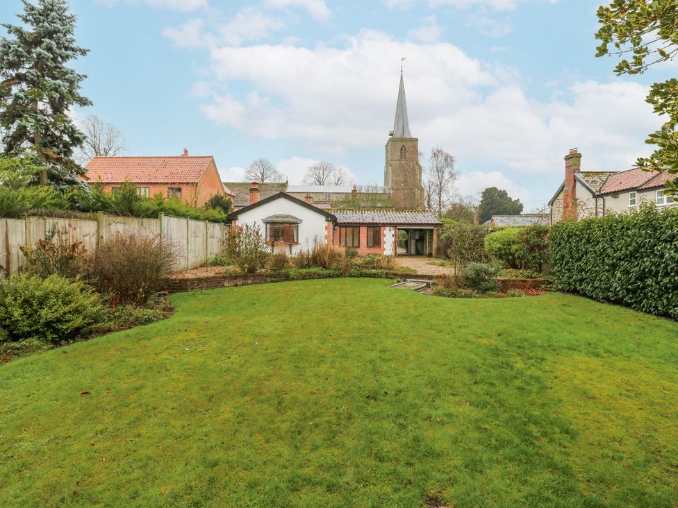 A garden with a house and church in the background at The Pantiles in Banham