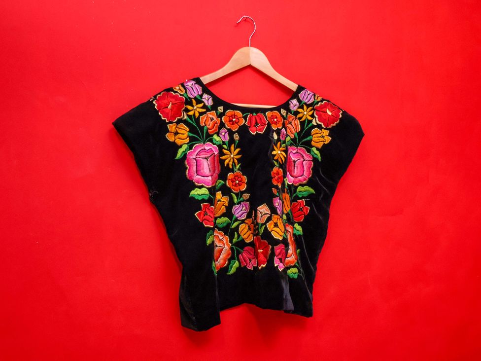 An embroidered blouse displayed on a hanger against a red background