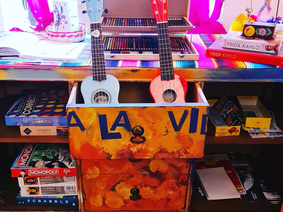 A living room with a desk featuring ukuleles and board games at Frida's Cottage in Whitby
