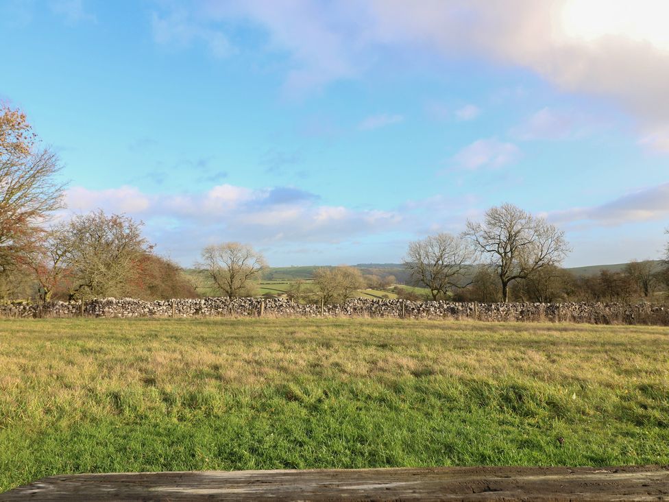 A view of a field with trees and a stone wall at Little Barn in Leek