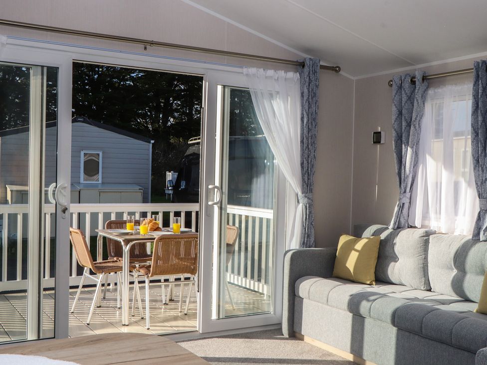 A living room with a sofa and glass doors leading to a deck at Caravan C31 at Landscove Holiday Park Brixham