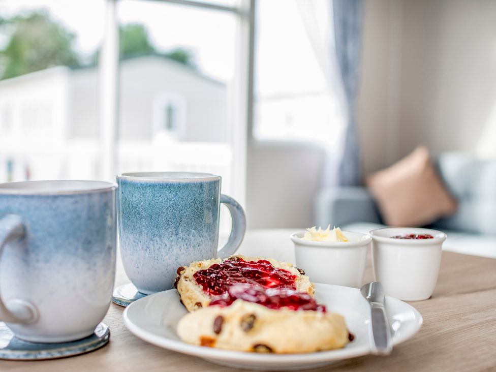 A dining area with mugs, a scone, butter, and jam at Caravan C32 at Landscove Holiday Park Brixham