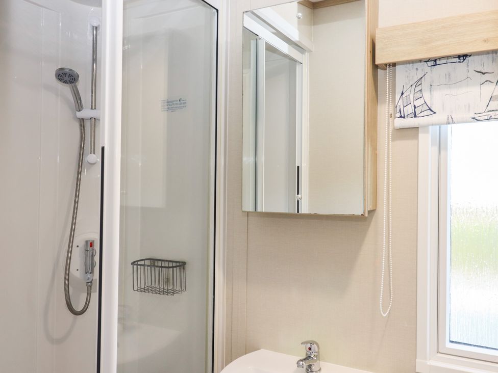 A bathroom with a shower, sink, and mirror at Caravan A24 at Landscove Holiday Park Brixham