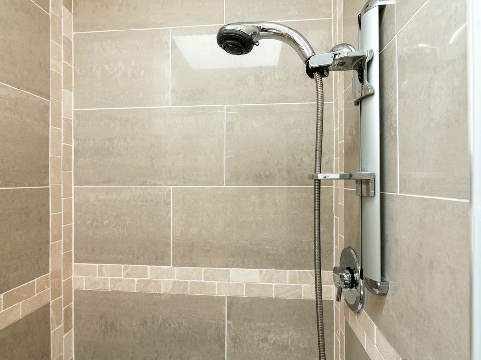 A shower with a chrome showerhead and tiled walls at Bank House Cottage Lancaster