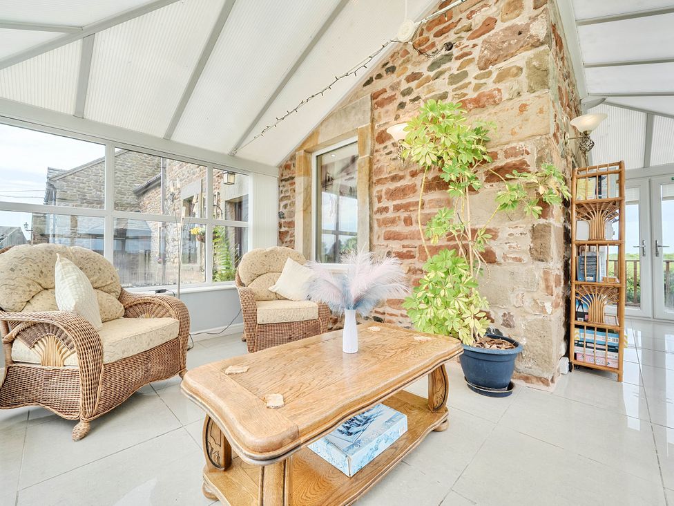 A conservatory with wicker chairs and a wooden table at Bank House Cottage in Glasson Dock
