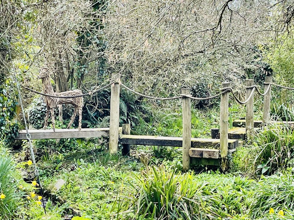 A wooden bridge with a sculpture in a wooded area at Mill Pond Cottage Widemouth Bay