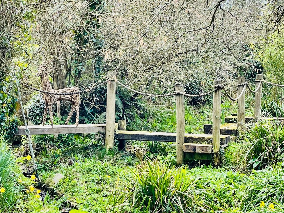 A bridge with a deer sculpture surrounded by greenery at Mill Pond Cottage in Widemouth Bay