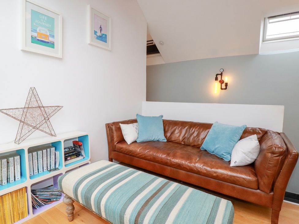 A living room with a leather sofa and books on a shelf at Meadow View in Bude