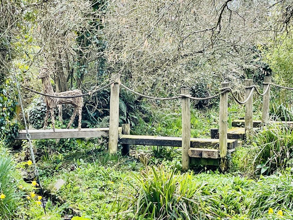 A wooden bridge with a sculpture in a garden at Meadow View in Widemouth Bay