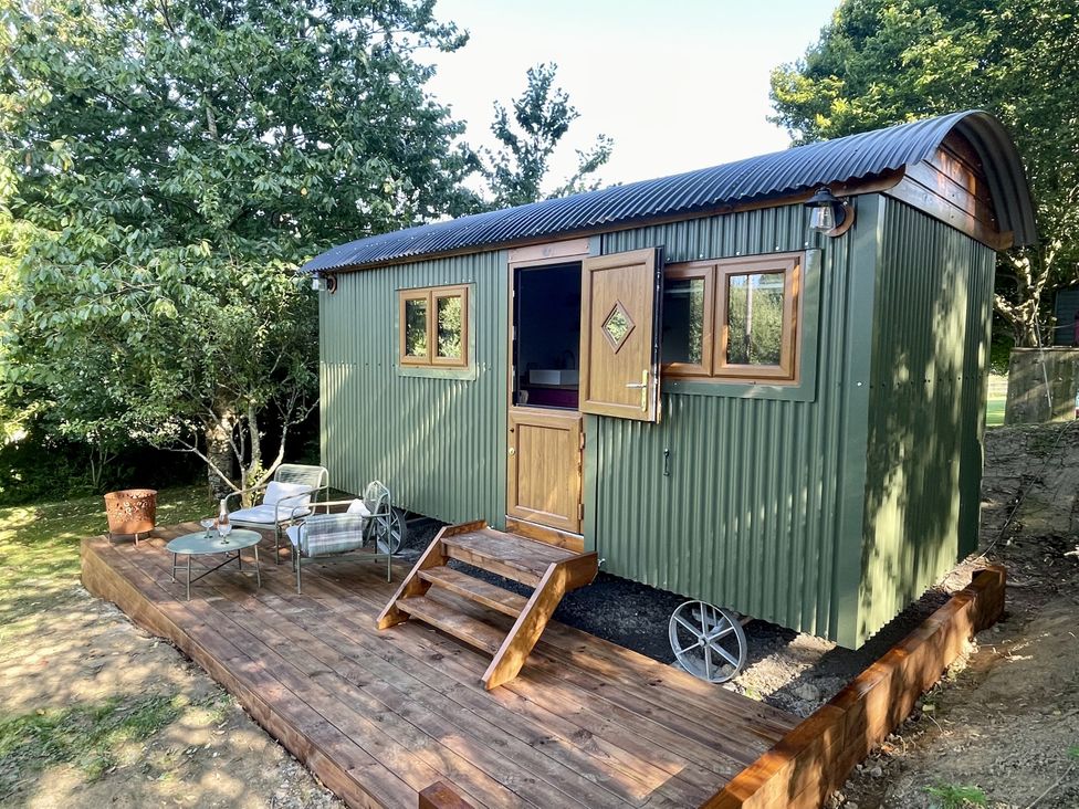 A shepherd's hut with a porch and outdoor seating at Bryar Widemouth Bay