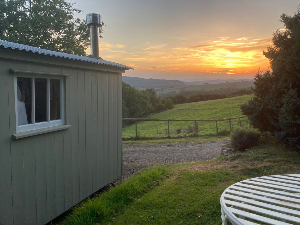 A hut with a chimney next to grass and a sunset view at Cosy Shepherd’s Hut Longhope