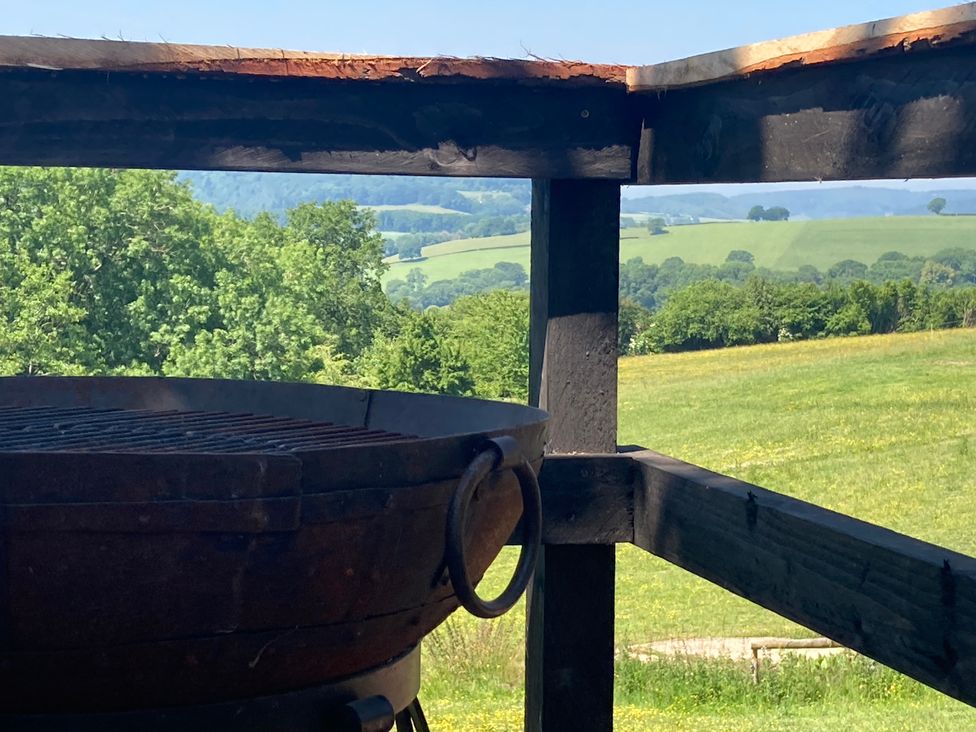 A grill and wooden structure with a view of greenery and hills at Cosy Shepherd’s Hut in Longhope