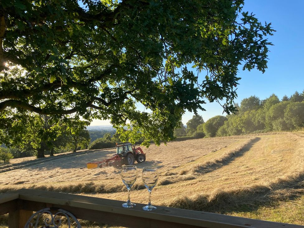 A tractor working in a field with glasses on a table at Cosy Shepherd’s Hut in Longhope