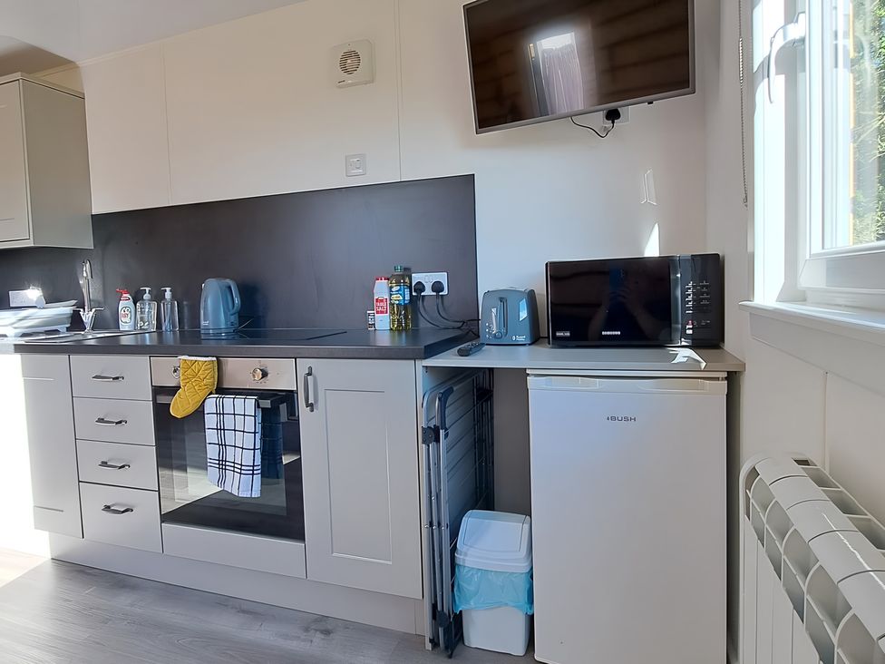 A kitchen with a sink, oven, kettle, toaster, microwave, and fridge at The Posh Bothy 2 Roy Bridge