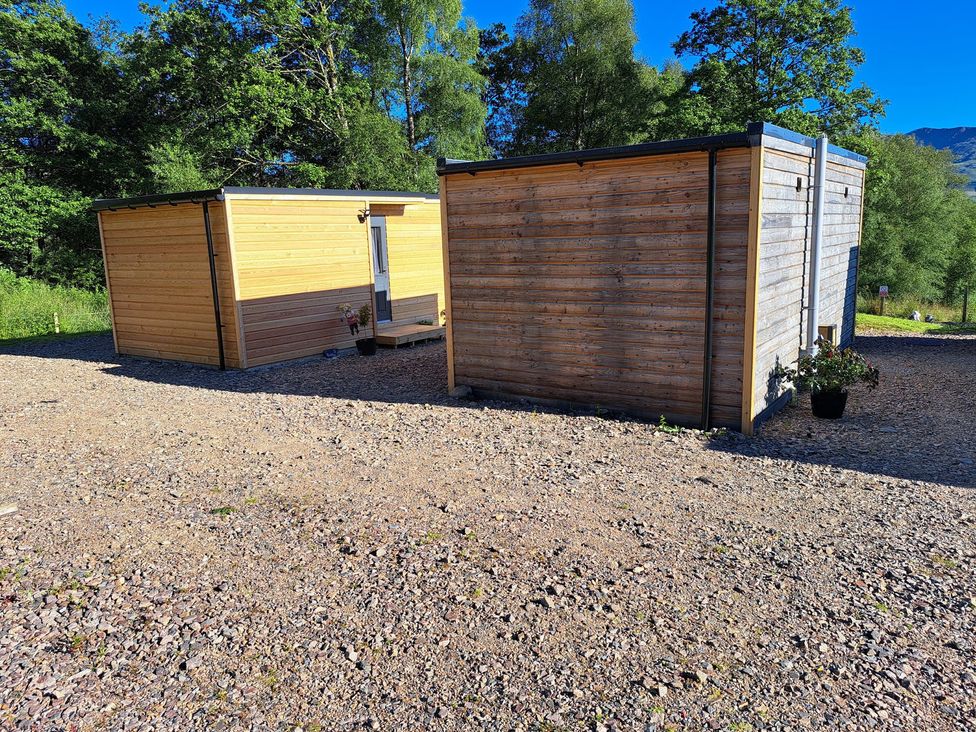 Two wooden cabins with a gravel area at The Posh Bothy 2 in Roy Bridge