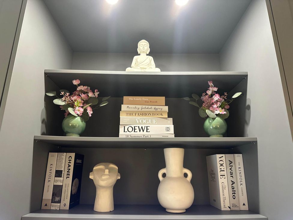 A shelf with books, vases, flowers, and a Buddha statue at Apartment 2 Preston, Lancashire