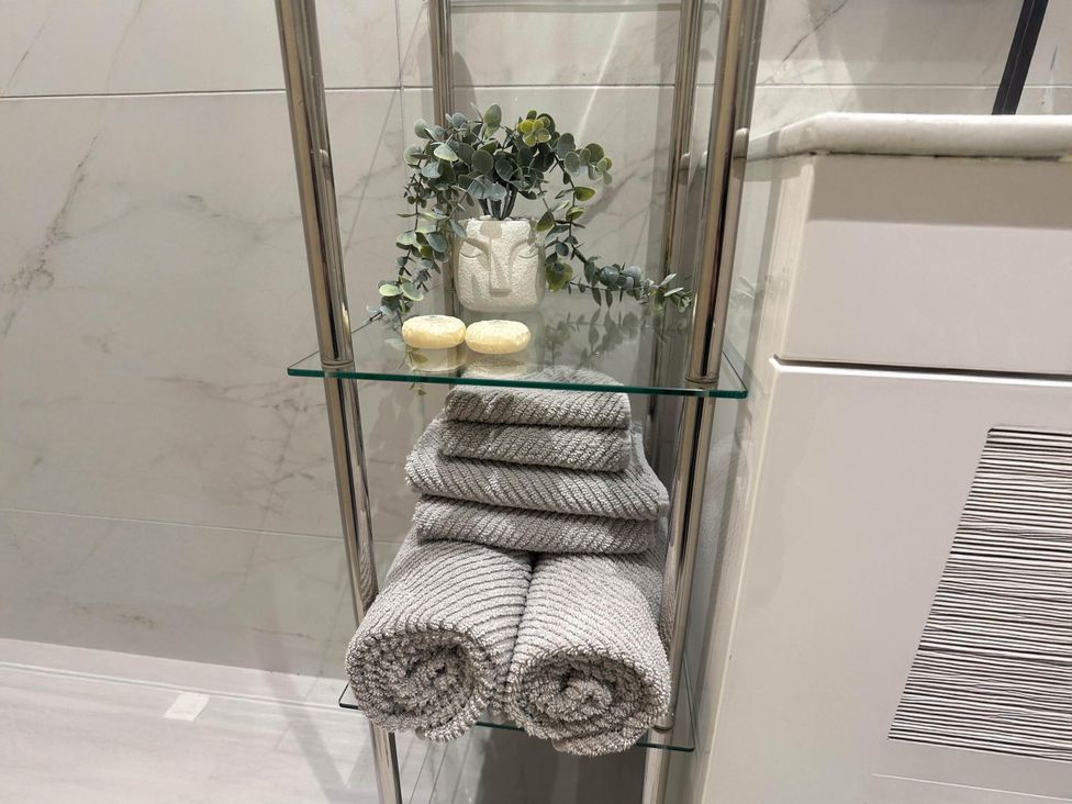A bathroom shelf with rolled towels, a plant, a decorative pot, and soap at Apartment 2 Preston, Lancashire