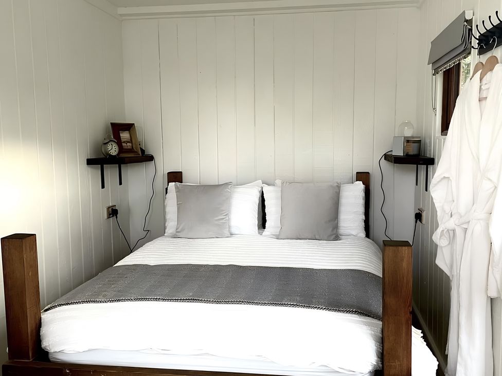A bedroom with a bed, pillows, clock, and shelves at Trethowels Hidden Huts in St. Austell