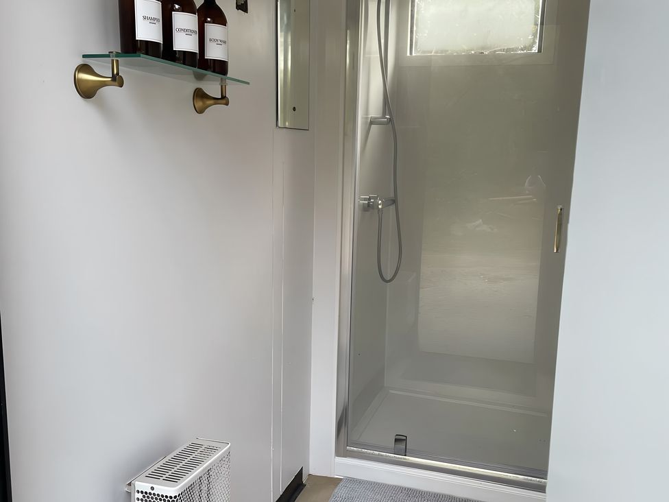 A bathroom with a shower and shelf holding toiletries at Trethowels Hidden Huts in St. Austell