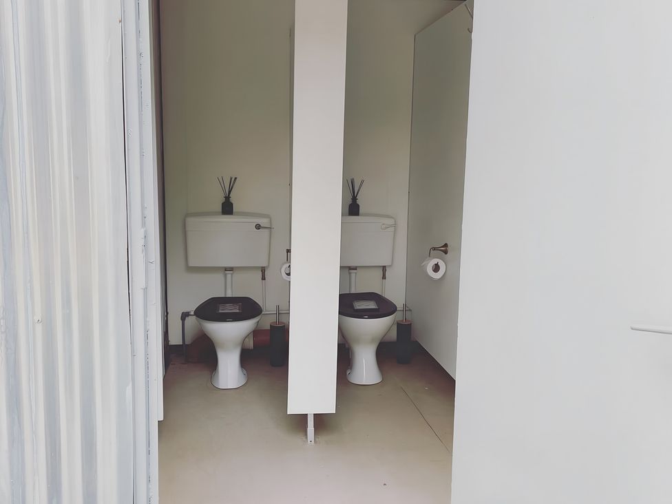 A bathroom with two toilets and a partition at Trethowels Hidden Huts in St. Austell